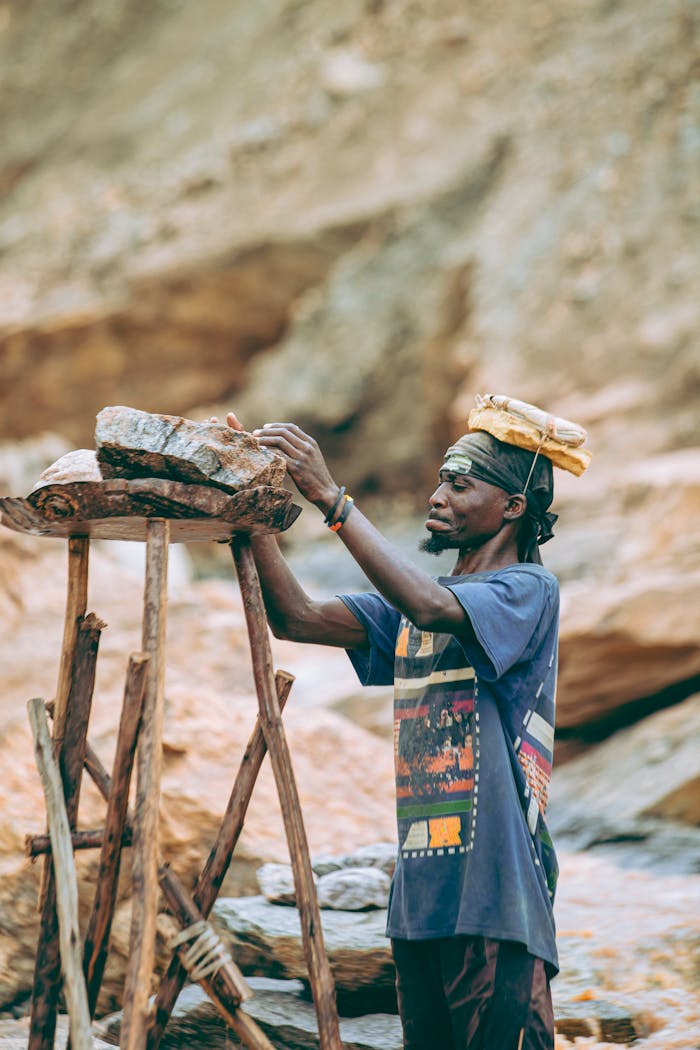 A miner in traditional attire working with stones in an outdoor quarry setting.